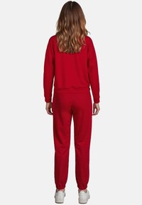 Červená mikina a kalhoty z měkké tkaniny. Úzký střih s ribbenými manžetami. Bílé tenisky doplňují outfit.