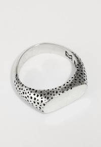 Sterling silver žiedas su lygiu, blizgiu juostele, kuriame yra juodų taškų raštai, siaurėjantys iki plokščios, opalinės baltos akmens apdailos.