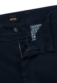 Tumši zili bikses ar rāvējslēdzēja atvēršanu, pogu aizdari un kabatu detaļām. Satur mīkstu tekstūru un "BOSS" logotipa birku iekšpusē.