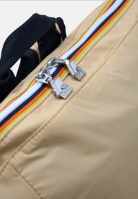 Beżowa torba o gładkim wykończeniu z tekstyliów, z wielokolorowym akcentem zamka błyskawicznego z metalowymi uchwytami oraz czarnym paskiem u góry.