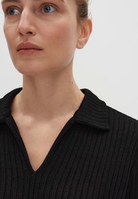 Zwarte geribde gebreide pullover met een V-hals en een gestructureerde kraag, die een textuurgeweven stof en een getailleerd ontwerp laat zien.