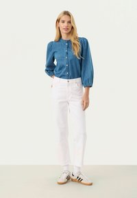 Ljust blå denimskjorta med puffärmar, kombinerad med vita högmidjade byxor och beige sneakers med svarta ränder.