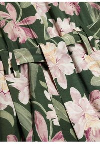 Tissu vert avec de grands imprimés floraux roses et blancs comprenant des plis pliés et des bandes ou sangles en tissu à travers la surface.