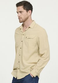 Lichtbeige langarm overhemd met een button-down kraag, borstzak en subtiele textuur. Voorzien van knopen aan de voorkant en een relaxed fit.