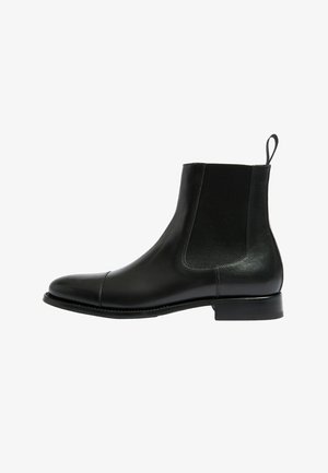 Bottine en cuir noir avec des panneaux élastiques sur les côtés, bout arrondi et un petit talon empilé. Elle dispose d'une languette pour un enfilage facile.