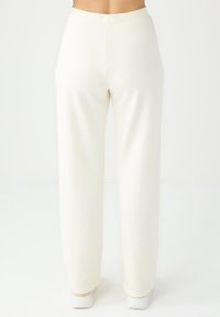 Pantalons larges crème en tissu doux, avec une texture lisse et une taille haute, de couleur unie et sans motifs visibles.