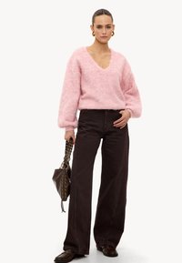 Pull rose duveteux à col en V, associé à un pantalon large marron taille haute. Accessoirisé d'un sac foncé avec des accents dorés.