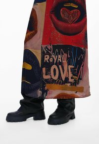 Gonna grafica multicolore con labbra e testo "ROYAL LOVE", caratterizzata da una texture liscia e colori vivaci. Abbinata a stivali neri robusti.