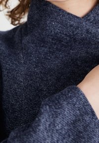 Marineblauer strukturierter Stoff mit einer weichen Oberfläche, der einen hohen Kragen und enge Ärmel aufweist und ein dezentes gewebtes Muster betont.
