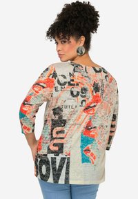 Haut ample et multicolore en tissu léger. Il présente des motifs graphiques audacieux en noir, orange et turquoise. Manches trois-quarts.