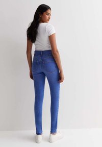 Chude niebieskie dżinsy z wysokim stanem, tylnymi kieszeniami i gładką fakturą, połączone z dopasowaną białą koszulką i białymi trampkami.