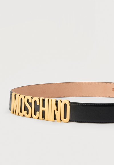 Μαύρη δερμάτινη ζώνη με μεγάλα χρυσά γράμματα που σχηματίζουν τη λέξη "MOSCHINO" ως λεπτομέρεια αγκράφας σε ουδέτερο φόντο.