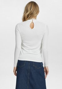 Witte blouse met lange mouwen en een kantenkraag, met een sleuf aan de achterkant. Gecombineerd met een donkerdenimrok met achterzakken.