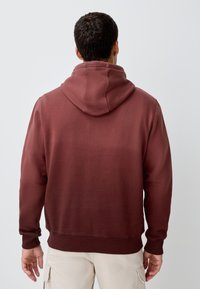 Sweat à capuche bordeaux avec une poche kangourou, des poignets et une taille côtelés. Tissu doux et coupe décontractée. Comprend une capuche réglable avec cordon de serrage.