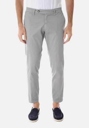 Uomo che indossa pantaloni aderenti grigio chiaro e scarpe slip-on blu navy, in piedi con le mani rilassate lungo i fianchi.