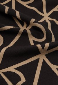 Čierna tkanina s béžovým geometrickým vzorom, ukazujúca záhyby a textúru.