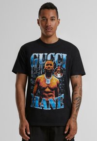 Black cotton t-shirt featuring a graphic print of a muscular figure with jewelry and the text "GUCCI MANE" in blue, with icy detailing.