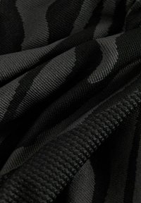 Svart tyg med ett strukturerat, vågigt mönster. Materialet verkar vara stickat och har olika nyanser av svart. Ytan har en något upphöjd textur.