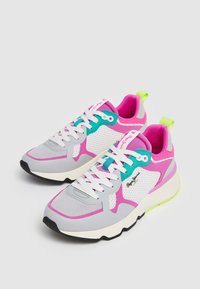 Sneakers grigi e bianchi con accenti rosa e turchese. Materiali in rete e sintetici, punta arrotondata, spesse stringhe bianche e una linguetta sul tallone di colore verde brillante.