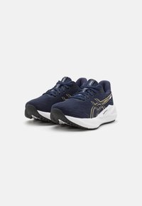 Baskets de sport bleu marine avec une tige en maille texturée, des accents dorés et une semelle légère blanche et noire, offrant un design moderne pour la course.
