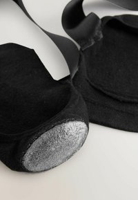 Juodos spalvos kojinės su švelniu, tekstūruotu paviršiumi. Kojinėms būdingas sidabro akcentas kulne ir persidengiančios juodos dirželiai, užtikrinantys tvirtą prigludimą.