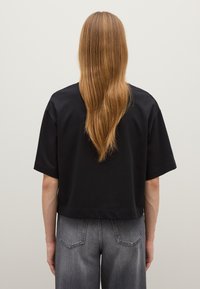 Zwarte cropped t-shirt met korte mouwen, van katoen, met een gladde textuur. Draagt bij hoge taille grijze denim broeken.