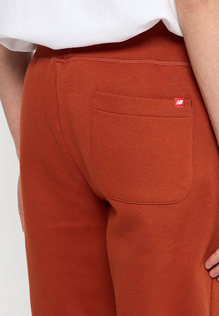 Rustkleurige sweatpants van zachte stof, met een achterzak en een klein rood merkhanger aan de zijkant, met een geribde tailleband.