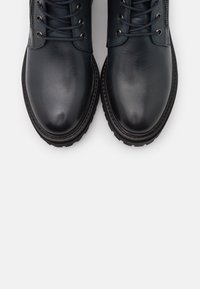 Stivaletti neri in pelle con punta rotonda, design con lacci, cerniera laterale, suola nera testurizzata e dettagli di cucitura sottili.