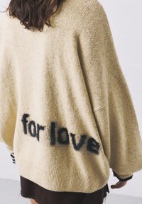 Pulover oversized bej cu tricot texturat, având inscripția "for love" în albastru închis pe spate. Manșete și tiv ribbed.