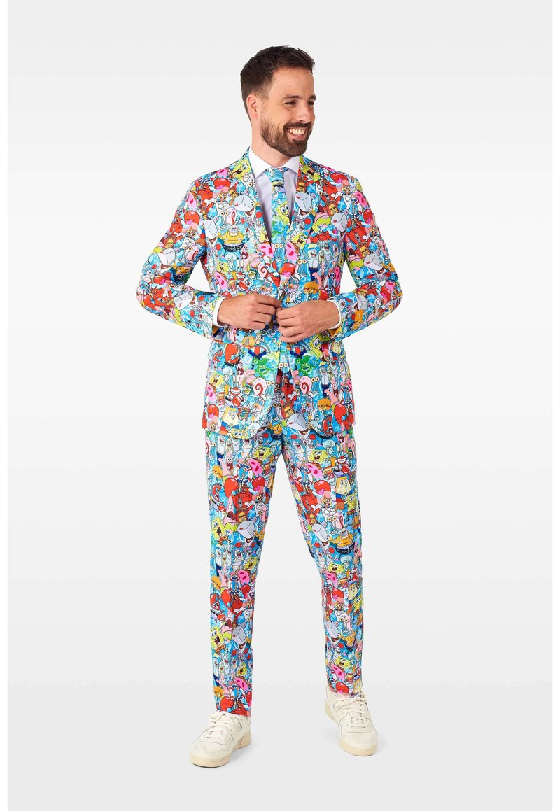 Colorful suit with cartoon patterns in red, blue, and yellow, featuring a fitted jacket and matching pants, worn with a light blue tie.