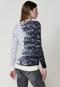 Knit pulover z gradientnim vzorcem v črni in beli barvi, z rebrastimi manšetami in robom, izdelan iz mehkega, teksturiranega materiala.