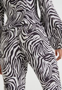 Zwart-wit zebra print stof met een peplumdetail, voorzien van lange mouwen en een gestructureerd oppervlak, dat de gedurfde, golvende patronen benadrukt.
