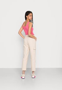 Top soquete rosa com textura canelada e calças cargo bege com bolsos laterais. Modelo usa sandálias brancas com toques rosa, vistos de trás.