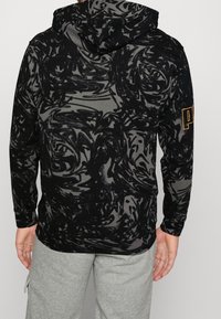 Hoodie w czarno-szarym wzorze z kapturem na sznurki, z długimi rękawami i haftowanym na lewym rękawie napisem "PUMA" w złotym kolorze.