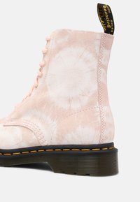 Botte en daim rose à lacets avec motif tie-dye blanc, semelle noire avec couture jaune, et boucle talon noire avec texte jaune.