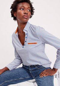 Chemise à manches longues à motifs en bleu et blanc avec des accents orange. Dotée d'un col, d'une patte de boutonnage et d'une poche poitrine.