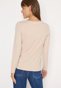 Beige langslijve top met een ronde hals en een soepele textuur, gecombineerd met blauwe denim jeans met een klassieke vijf-pocket ontwerp.