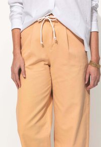 Des pantalons larges pêche clair avec une taille élastiquée dotée d'un cordon crème, poches latérales et un tissu en coton doux.
