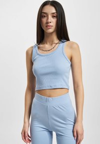Svetle modrý žebrovaný crop top s širokými ramínky, doplněný o odpovídající vysoké legíny. Textura vypadá měkce a elasticky.