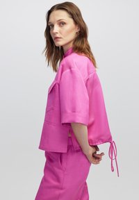 Korte mouwen roze blouse van een lichtgewicht stof, met een zak, verstelbare zoom met trekkoord en zijsplitten voor ventilatie.