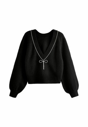 Frau trägt einen schwarzen Strickpullover mit tiefem V-Ausschnitt, der am Rand mit einer funkelnden Strass-Schleifenverzierung akzentuiert ist.
