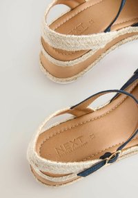 Tan nahkahengelliset espadrilles-kengät, joissa on tummansiniset hihnat, juuttikääreinen pohja ja teksturoitu sisäpohja, jossa on "NEXT"-logo.