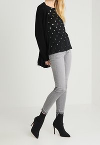 Svart tröja med texturerad stickdesign, prickigt mönster med metalliska accenter, kombinerad med grå skinny jeans och svarta ankelboots i sockmaterial.