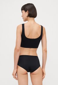 Black cotton bralette with lace trim, square neckline, and wide straps, paired with black high-waisted briefs featuring a smooth texture.