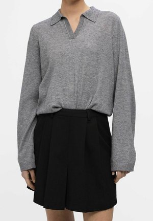 Grå strikket pullover med V-hals og krave, parret med en højtaljet sort plisseret nederdel, der viser tekstureret stof og rene linjer.