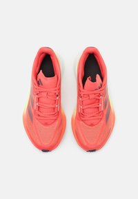 Chaussures de course corail avec une tige en mesh, doublure noire, semelle vert clair et accents roses. Présente trois bandes noires sur le côté.