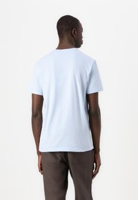 Ljusblå kortärmad t-shirt i mjukt tyg, med rundad halsringning och en avslappnad passform. Buren med bruna byxor.