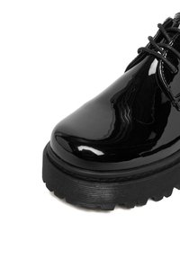 Mustast lakknahast king ümarate varvastega, tekstuurse tallaga ja mustade paeltega; läikiv pind peegeldab valgust; pakse taldadega disain.