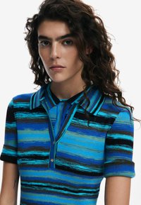 Polo a maglia con un motivo a strisce multicolori blu e verde, maniche corte e colletto con bottoni per la chiusura.