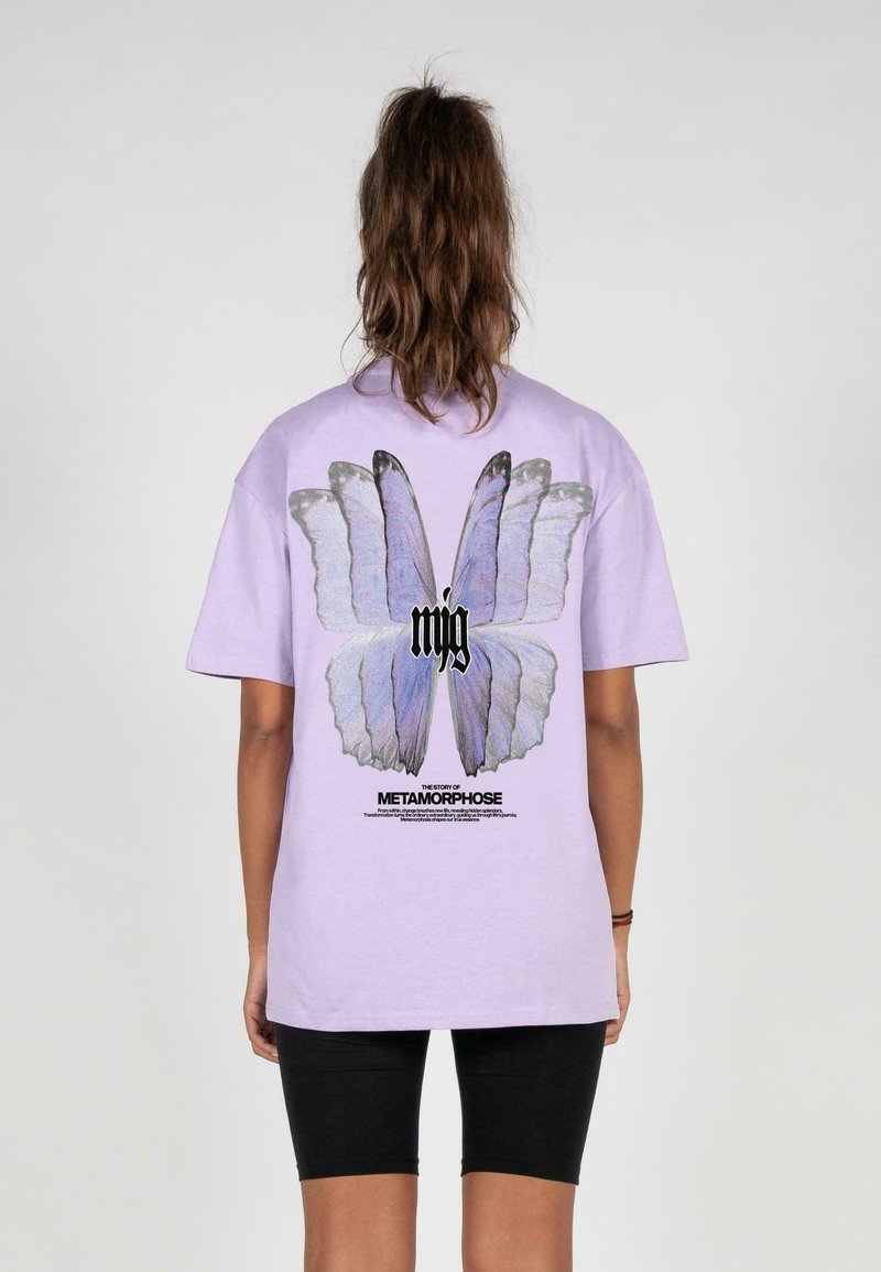 Lys lilla t-shirt med et stort sommerfuglegrafik på ryggen og sort tekst nedenfor. Stoffet ser blødt ud; casual, afslappet pasform.